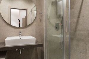 Ein modernes Badezimmer mit einem rechteckigen Waschbecken, einem runden Spiegel und einer Duschkabine aus Glas.