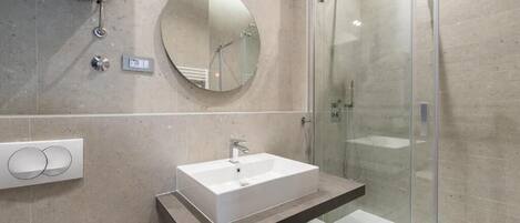 Une salle de bain moderne avec un lavabo rectangulaire, un miroir rond et une cabine de douche en verre.