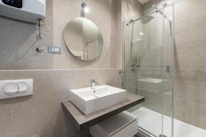 Ein modernes Badezimmer mit einem rechteckigen Waschbecken, einem runden Spiegel und einer Duschkabine aus Glas.