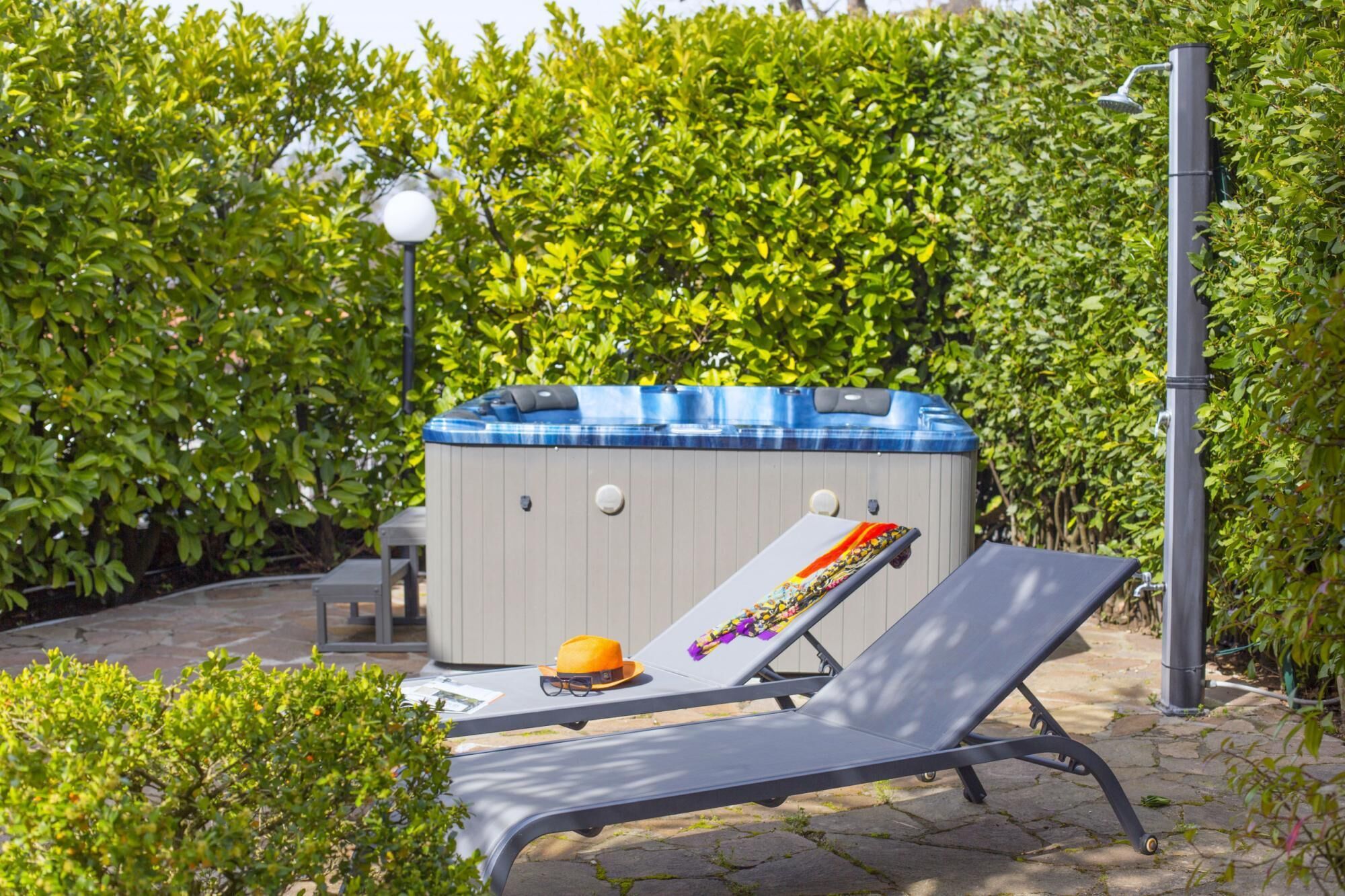 A hot tub with a blue cover, a lounge chair, and a small table with a hat and sunglasses.