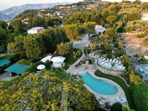 Vue aérienne d’un complexe hôtelier doté d’une piscine, de chaises longues et surplombant un paysage montagneux.