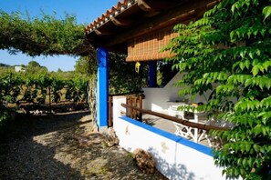 A building with a blue and white exterior, a wooden balcony, and a garden area with green foliage. - MUSEDDU HOUSE 2 (Cardeddu)