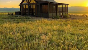 A modern house with a large glass window, a chimney, and a view of the landscape. - Three Peaks Ranch (Westcliffe)