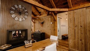 A rustic interior with a wooden ceiling, a large wall clock, a fireplace, and a dining area with a wooden table and white chairs. - Three Peaks Ranch (Westcliffe)