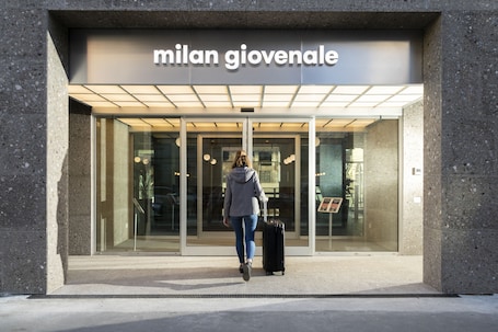 A building entrance with the sign "milan giovenale" and a person with a suitcase.