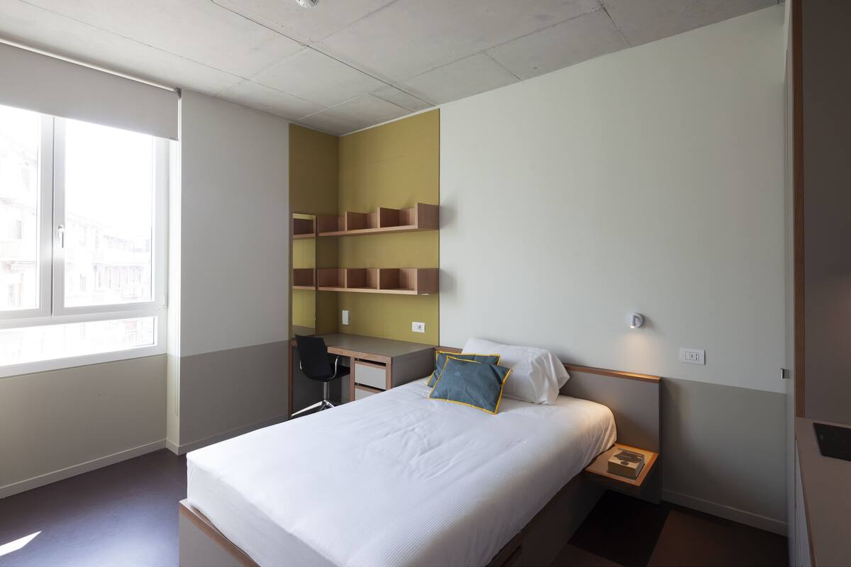 A hotel room with a bed, a desk, and built-in shelves.