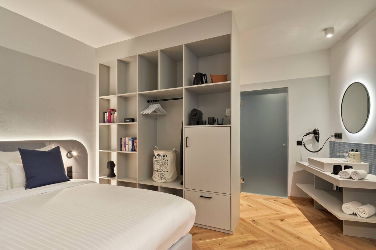 Ein modernes Schlafzimmer mit einem großen Bett, einem eingebauten Kleiderschrank und einem Badezimmer mit Spiegel und Waschbecken.