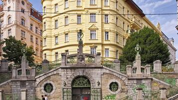 Ein historisches Gebäude mit aufwendiger Architektur, einem zentralen Eingang mit Statue und einer Treppe, die zu einer oberen Ebene führt.