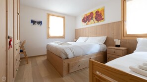 A bedroom with a wooden bed, a wooden wardrobe, a small bedside table, and a window.