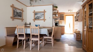 A cozy dining area with wooden furniture, a table with a blue tablecloth, and a view of the kitchen in the background.