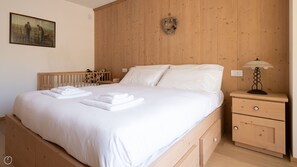 A neatly made bed with white linens and towels, a wooden headboard, a nightstand with a lamp, and a painting on the wall.