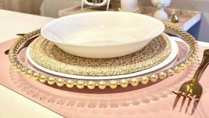 A dining table with a white plate, gold decorative plate, and a gold fork.