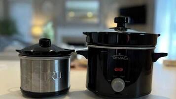 Une cuisine avec une mijoteuse noire et une casserole en acier inoxydable posée sur le plan de travail.