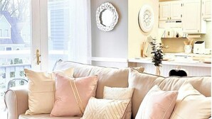 A living room with a beige sofa, a decorative wall plate, and a kitchen area with cabinets and a countertop.