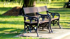 Een parkbank met een metalen frame en houten zitvlak, gelegen aan een geplaveid pad.