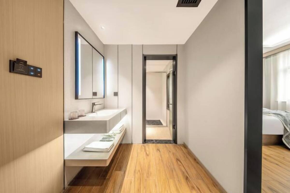 Een moderne hotelgang met een houten vloer, een witte, wandgemonteerde wastafel en een spiegel.