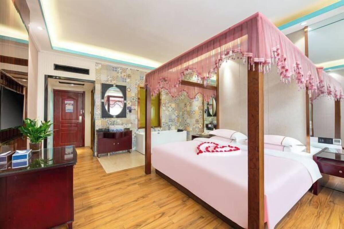 Een hemelbed met baldakijn, een receptiebalie, een spiegel en een badkamer met bad.