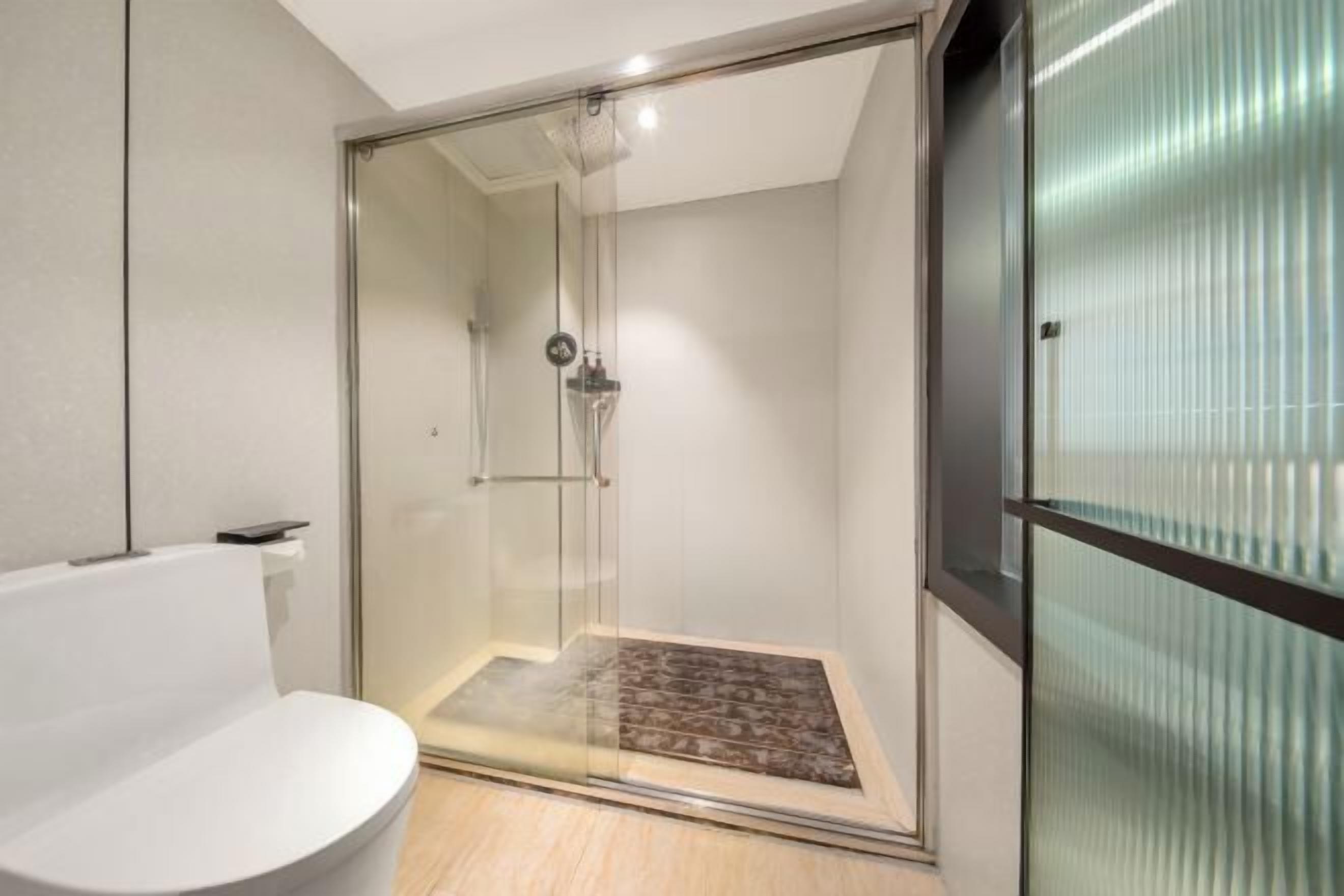 A modern bathroom with a glass-enclosed shower, a white toilet, and a wooden floor.