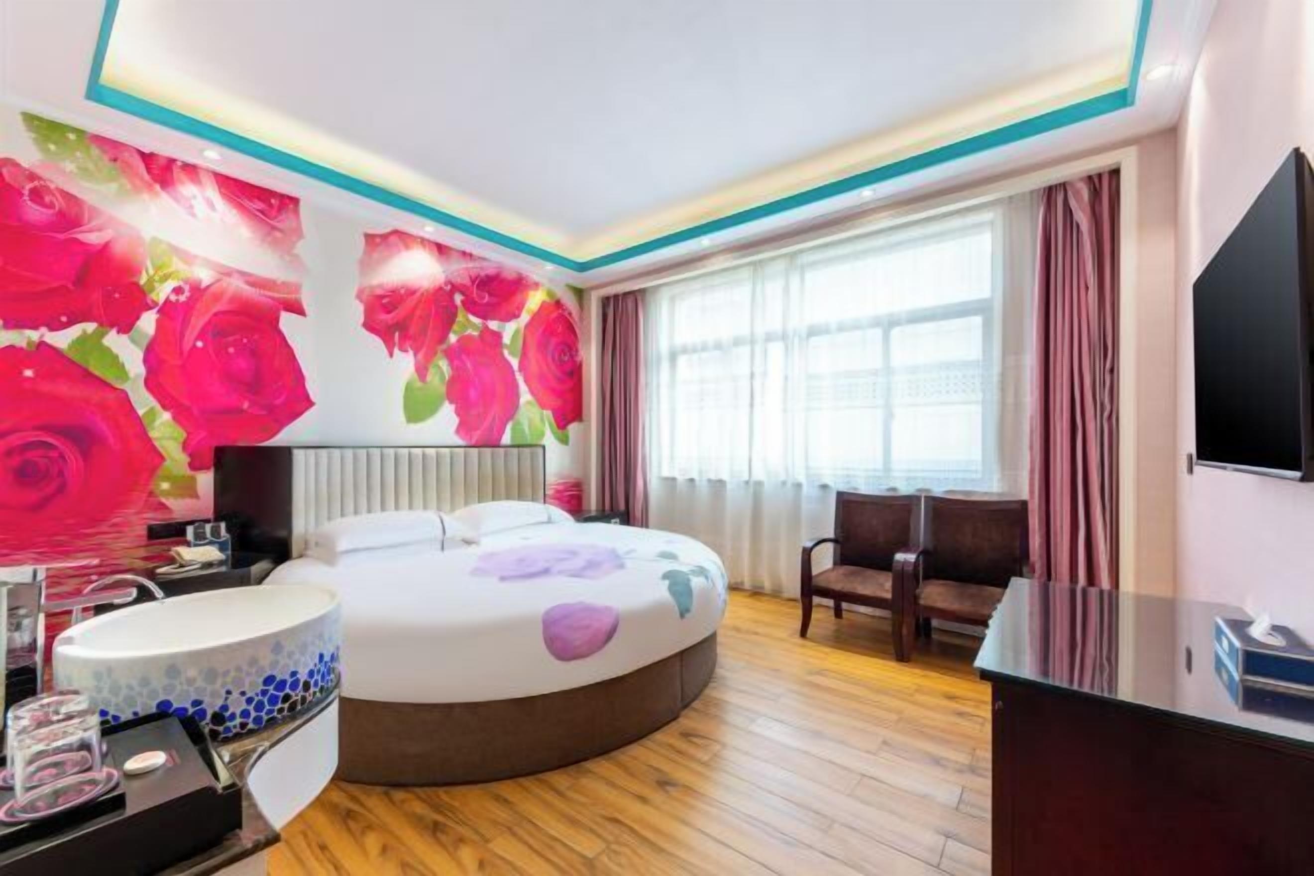 A hotel room with a large bed, a desk, a TV, a bathroom with a sink, and a window with curtains.