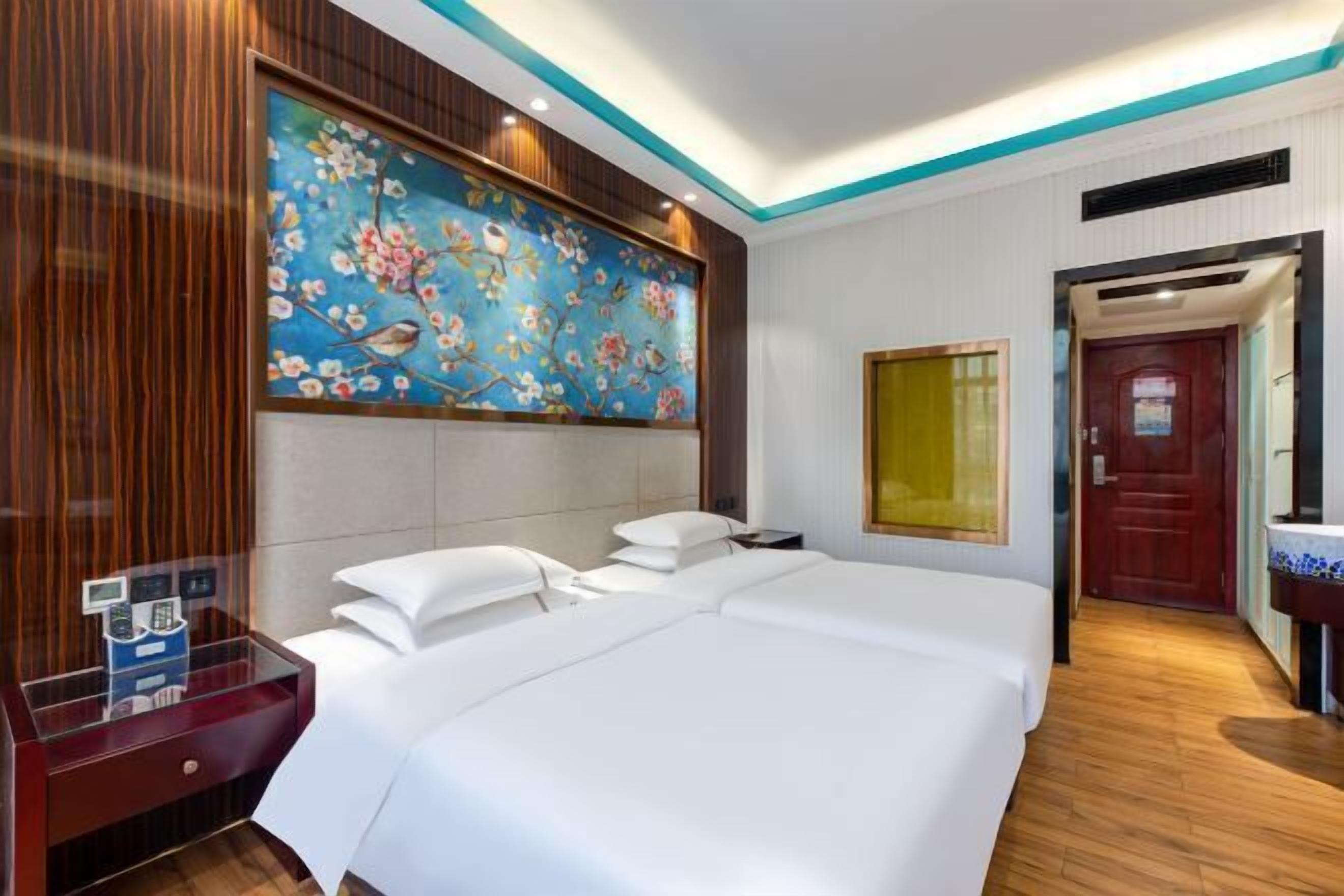 Ein Hotelzimmer mit zwei Betten, einem Holzkopfende, einem Gemälde mit Vögeln und Blumen sowie einem Holzboden.