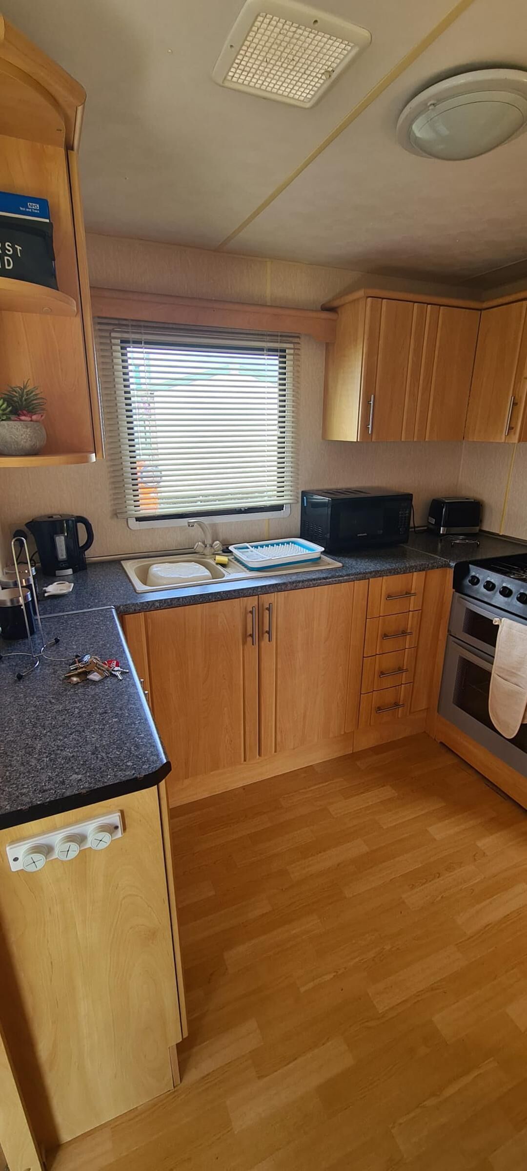 A compact kitchen with wooden cabinets, a microwave, a toaster, a sink, and a stove.