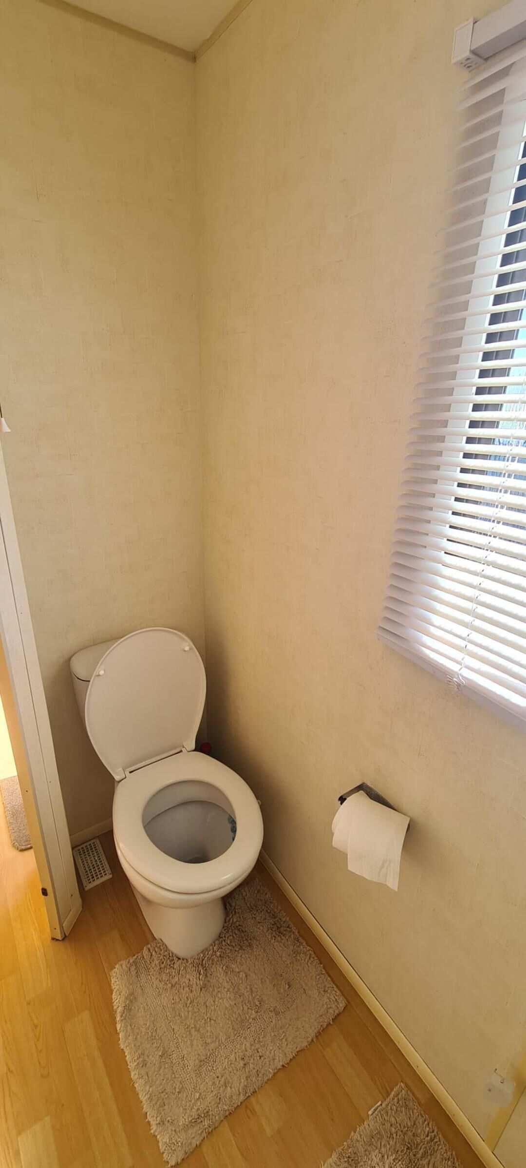 A small bathroom with a toilet, a towel rack, and a window with blinds.