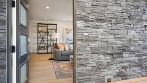 A modern living room with a stone wall, a sofa with cushions, a floor lamp, and a rug. - Casa Lua: Desert Color Lagoon + Beaches (St. George)