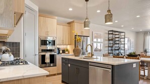 A modern kitchen with a central island, stainless steel appliances, wooden cabinets, and pendant lighting. - Casa Lua: Desert Color Lagoon + Beaches (St. George)
