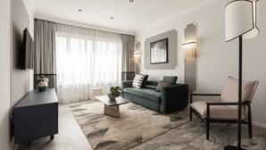 Una sala de estar moderna con un sofá oscuro, una mesa de centro, una lámpara de pie y un televisor sobre un mueble.