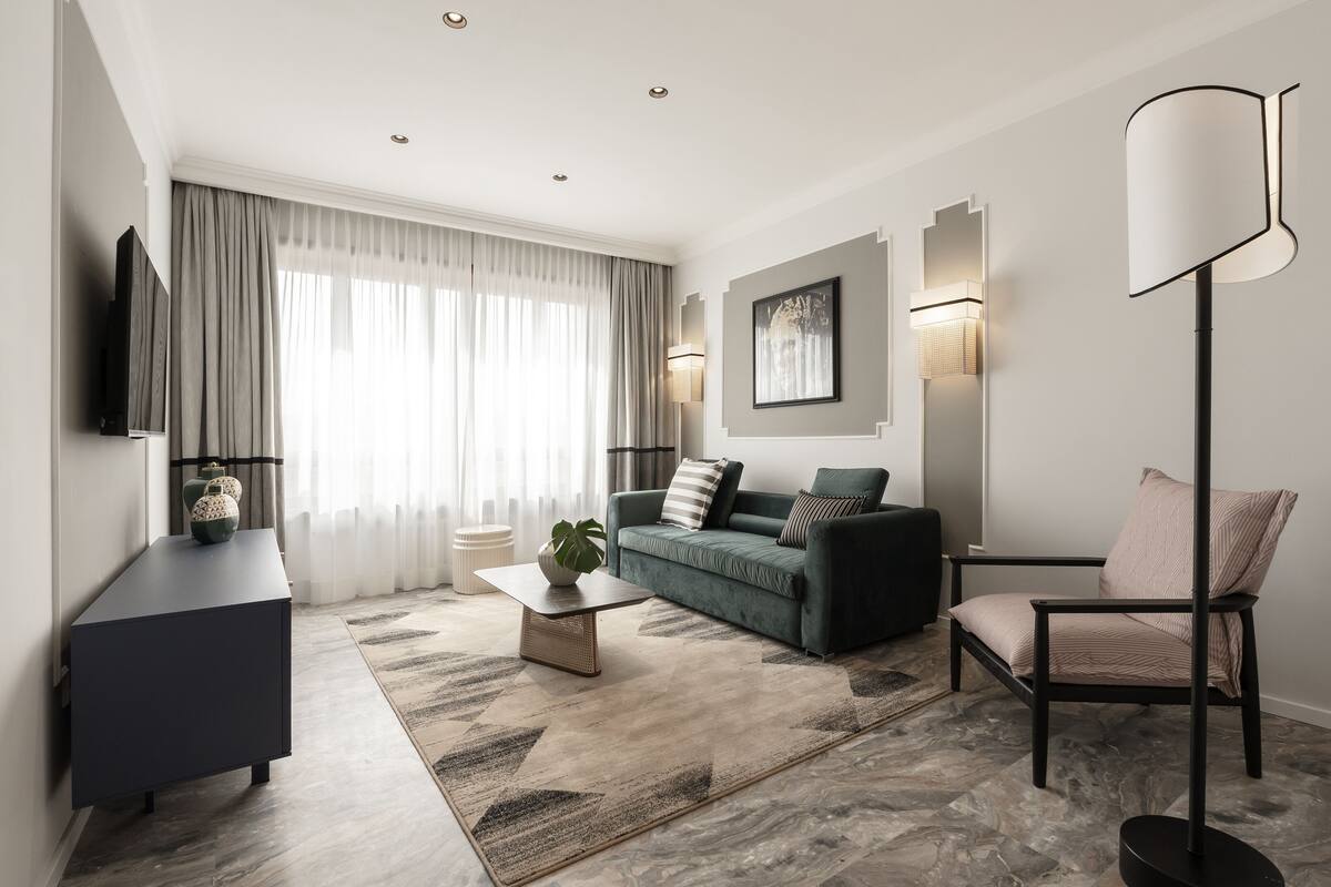 Una sala de estar moderna con un sofá oscuro, una mesa de centro, una lámpara de pie y un televisor sobre un mueble.