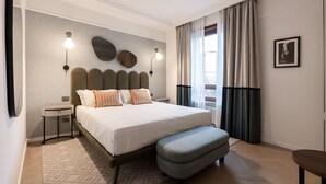 Un dormitorio moderno con una cama grande, mesitas de noche, un banco y vistas al exterior a través de una ventana con cortinas.