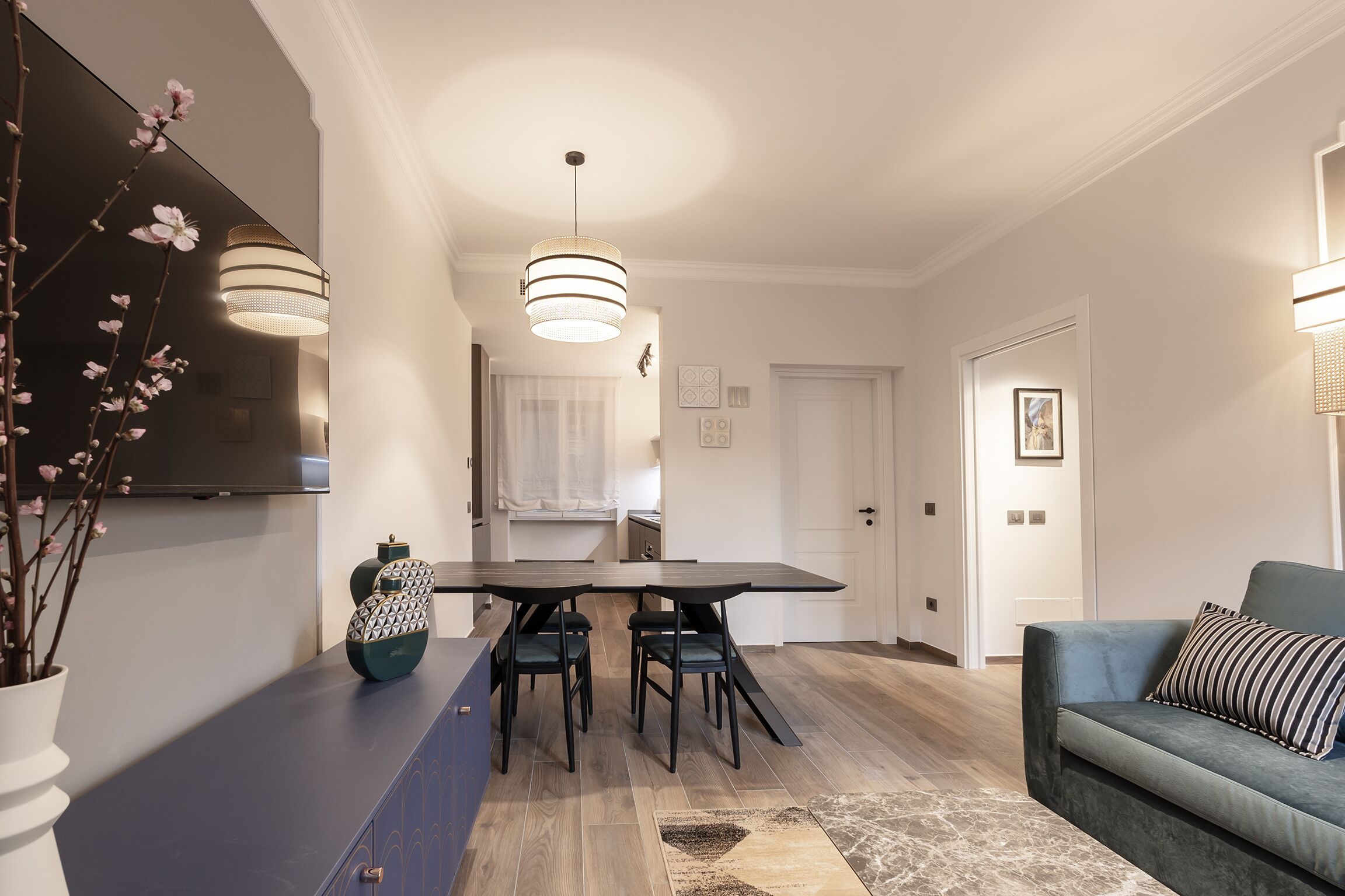 Ein modernes Wohnzimmer mit Esstisch, zwei Stühlen, einer Couch und einem an der Wand befestigten Fernseher.
