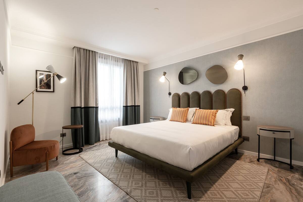 Un dormitorio moderno con una cama grande, una silla, una mesita de noche y una lámpara.