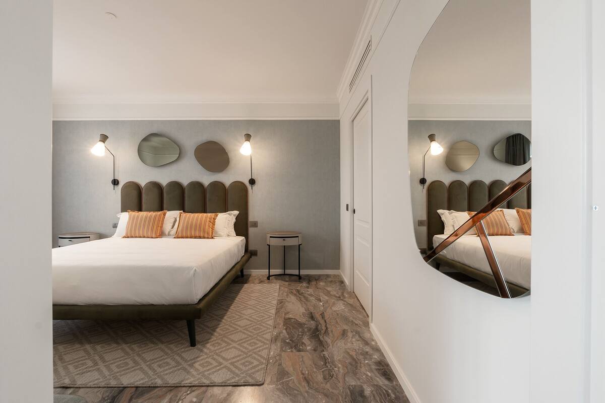 Un dormitorio moderno con cama, lámparas de noche, una mesita y un espejo.