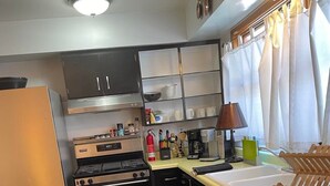 Eine kompakte Küche mit Kühlschrank, Herd und Geschirrspüler. Holzdielen, ein Teppich und ein Fenster mit Vorhängen gehören zur Ausstattung.