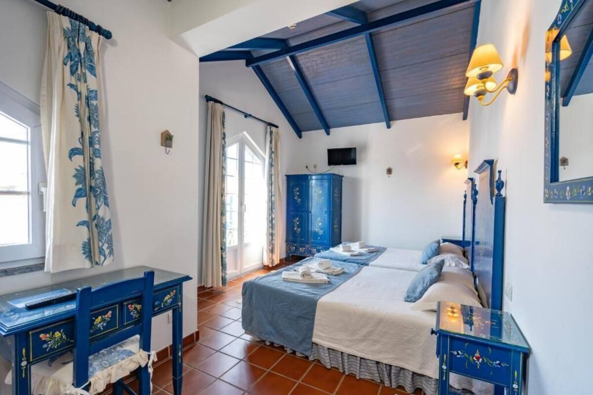 A bedroom with a bed, a desk, a wardrobe, and a window with curtains.