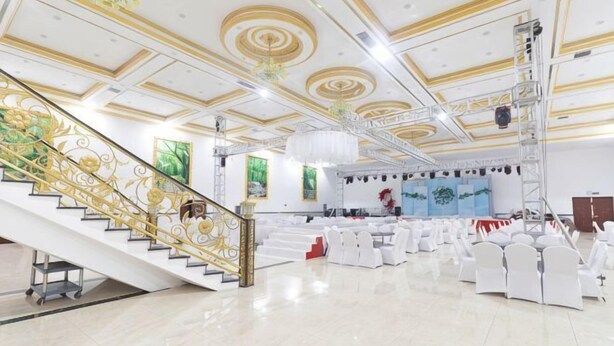 A spacious hall with a grand staircase, white chairs, and a stage with a blue backdrop. - Kingdom Hotel (Panjin)
