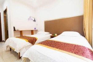Habitación de hotel con dos camas, cada una con ropa blanca y un corredor estampado. Hay una mesita de noche de madera entre las camas y un pequeño estante con objetos encima.