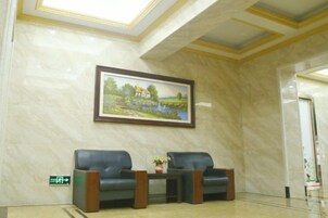 A lobby with marble walls, a framed landscape painting, two leather chairs, and a small table with a plant.