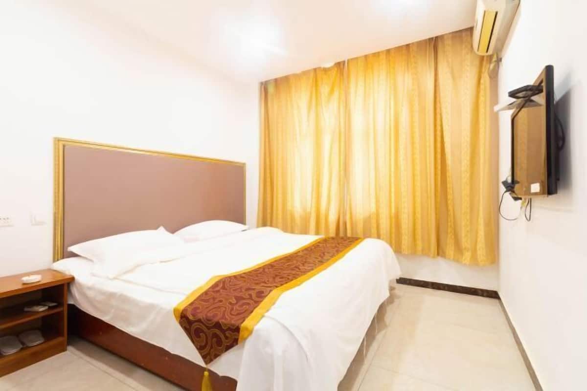 A hotel room with a bed, a wooden nightstand, a TV, and a window with curtains.