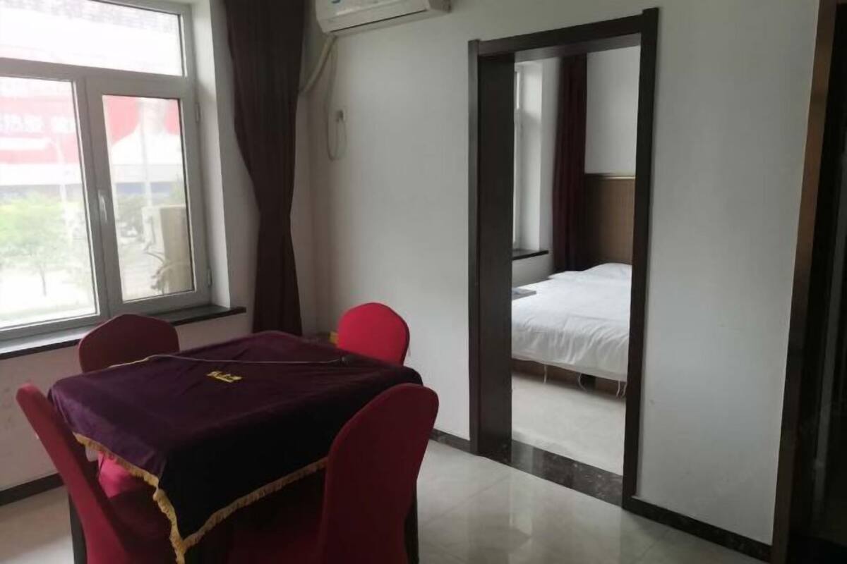 A hotel room with a bed, a table with a purple tablecloth, and red chairs.