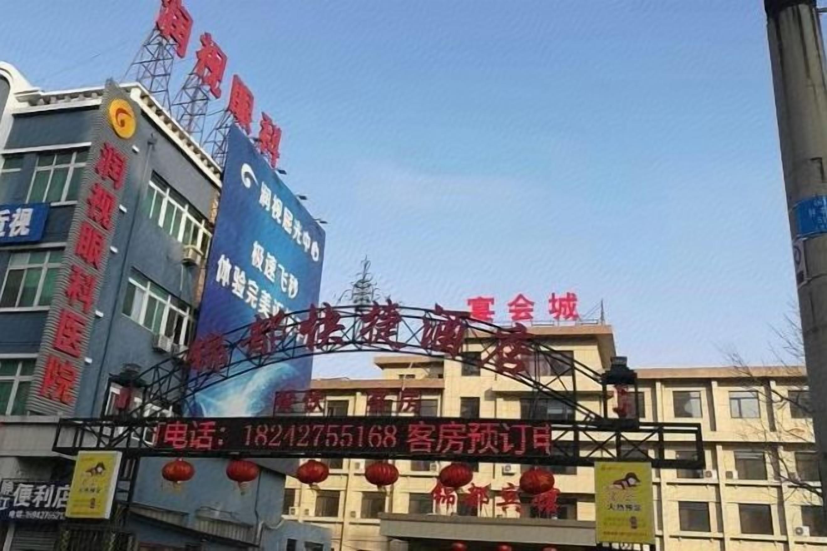 A hotel entrance with a blue sign, red lanterns, and a visible phone number.