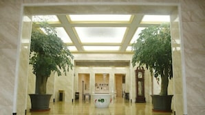 A spacious lobby with a high ceiling, marble flooring, and two large potted plants. - Kingdom Hotel (Panjin)