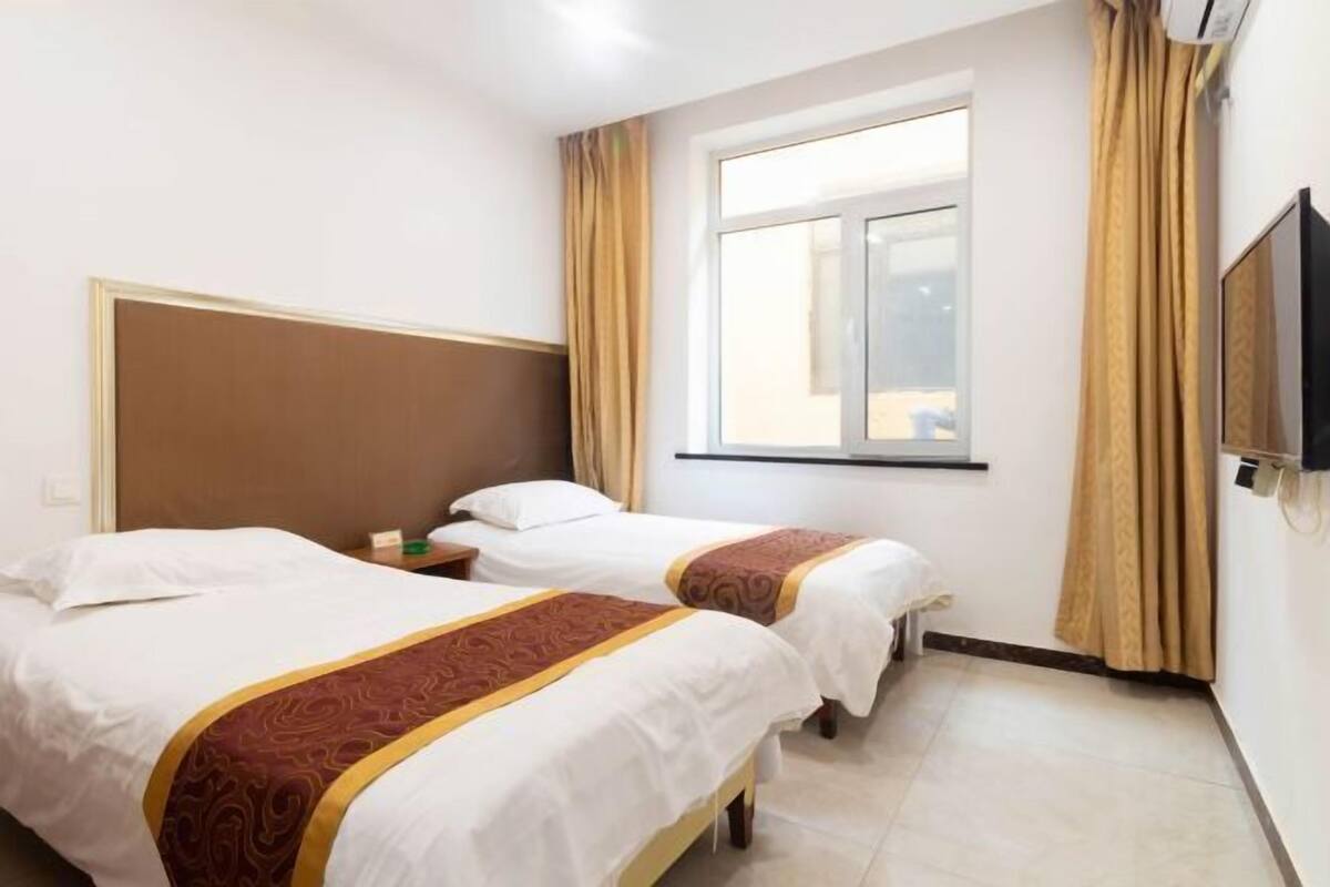 A hotel room with two beds, a window, a television, and a bedside table.
