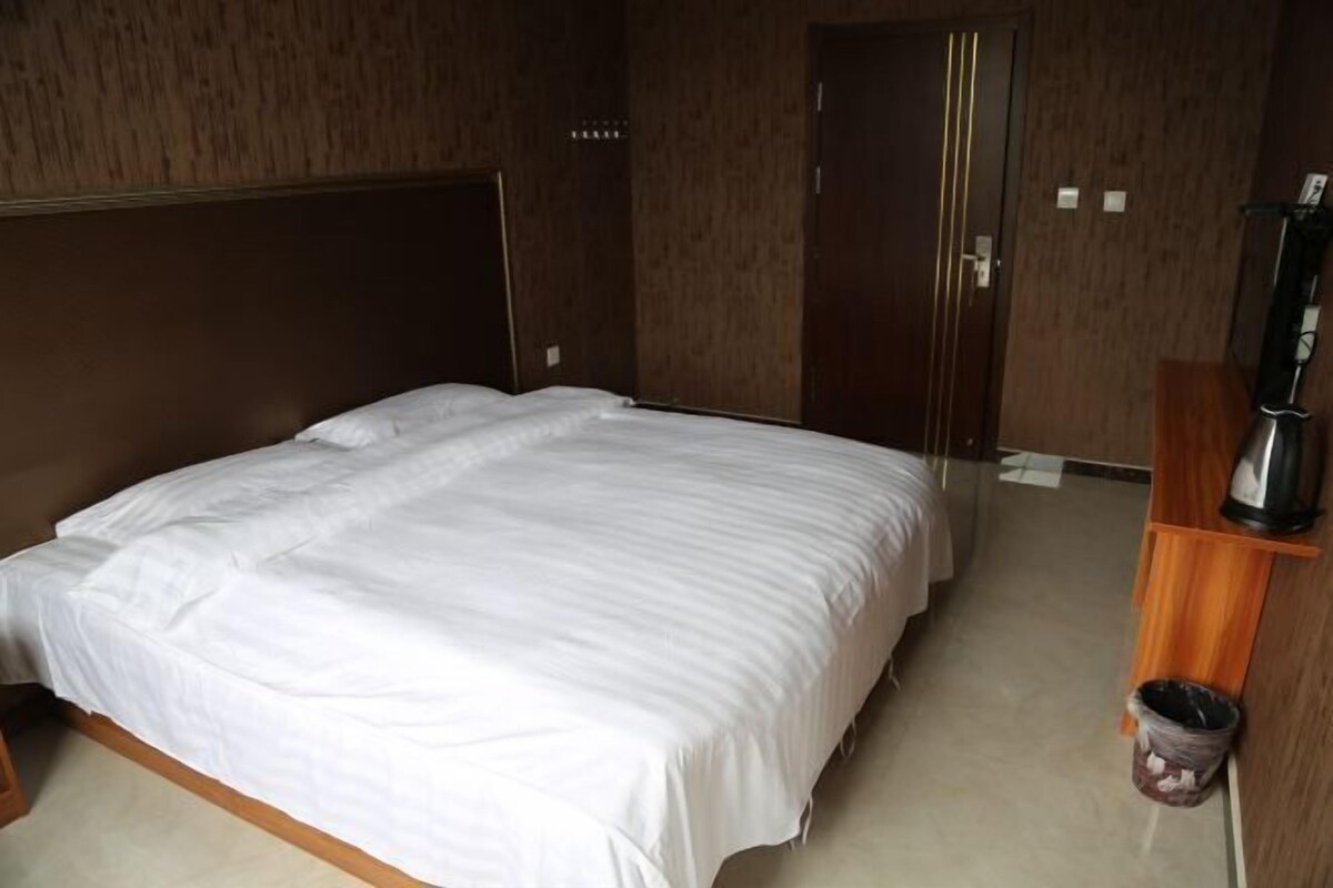 A hotel room with a large bed, wooden headboard, a wooden cabinet, and a trash bin.