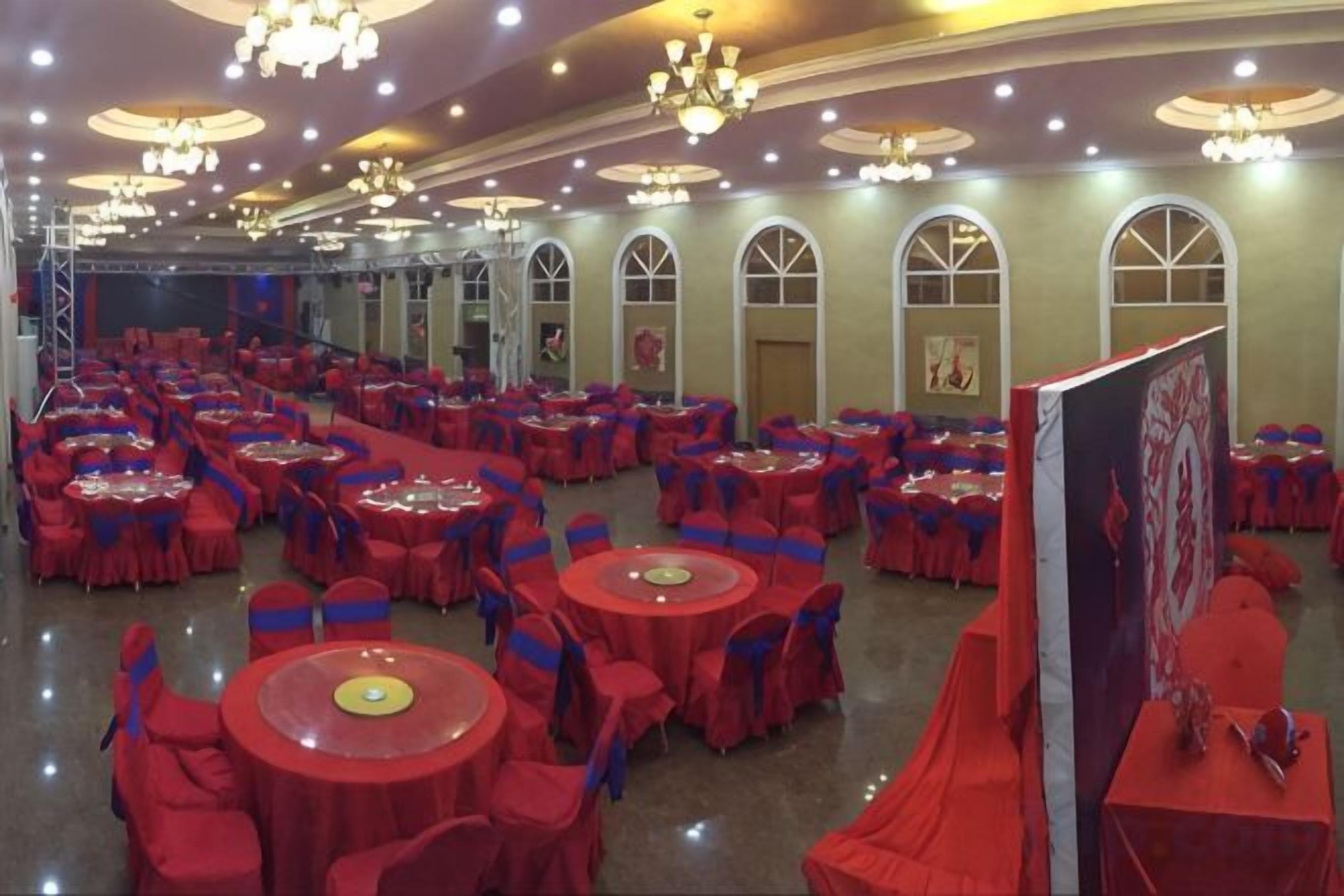 A banquet hall with round tables, red tablecloths, and blue chair covers.