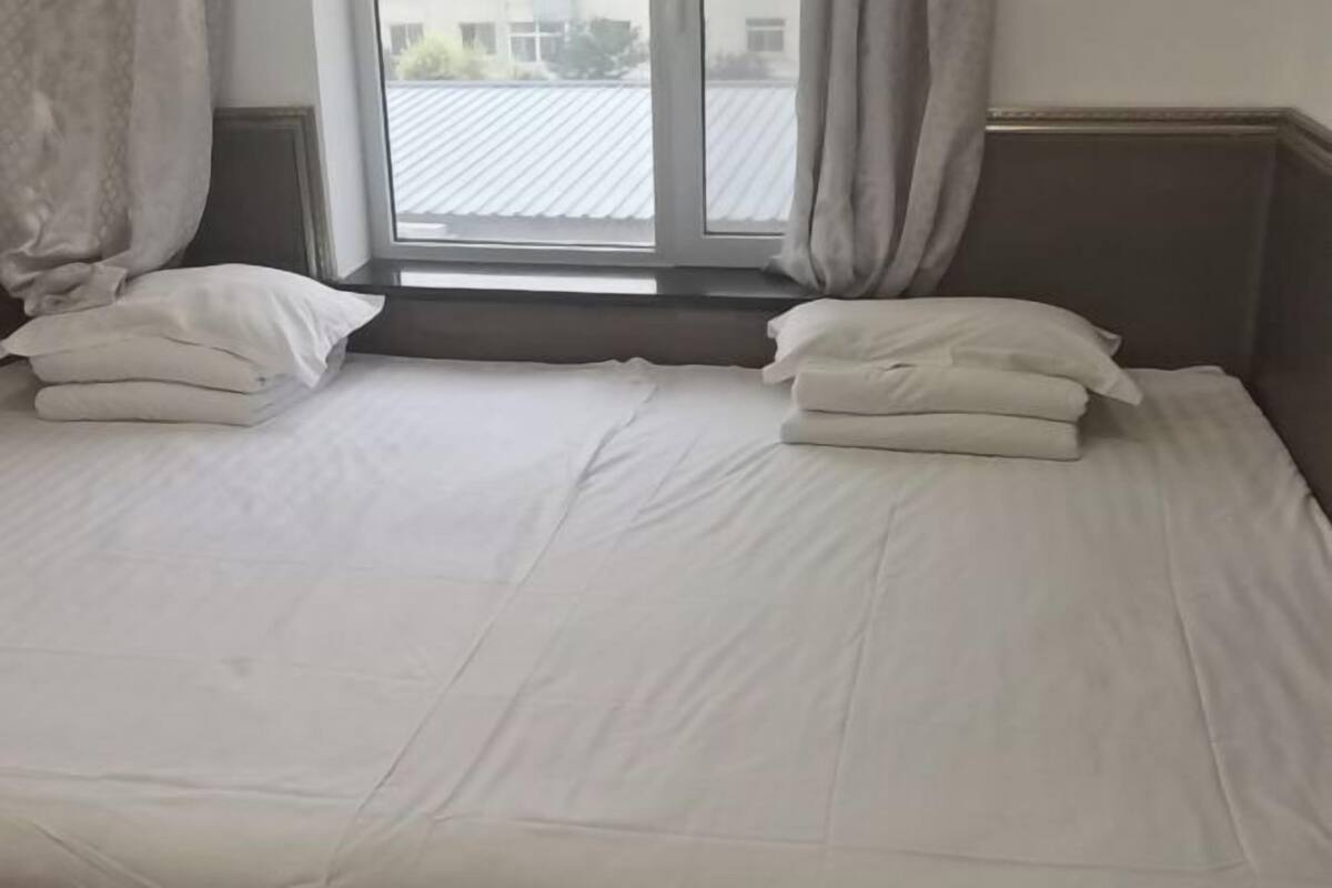 A bed with white bedding and pillows, a window with curtains, and a view of a building outside.