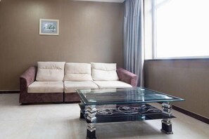 A living room with a glass coffee table, a beige sofa, and a framed picture on the wall.
