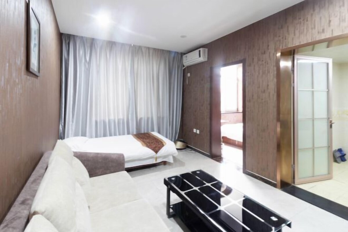 A hotel room with a bed, a sofa, a small table, and a sliding glass door leading to a balcony.