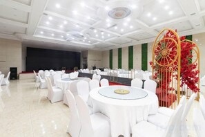 A banquet hall with round tables and white chairs, a stage, and a decorative red and gold structure. - Kingdom Hotel (Panjin)